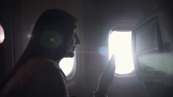 Menina senta-se no avião cabine de passageiros surf internet perto — Vídeo de Stock