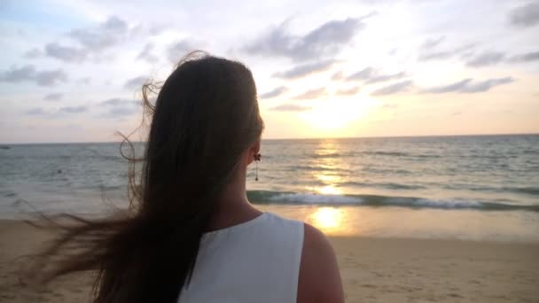 Жінка з довгим волоссям стоїть на океанічному пляжі у вітряний вечір — стокове відео