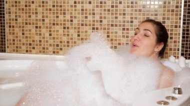 Kadın banyoda yatarken köpükle oynuyor.