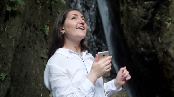 Mujer feliz sostiene el teléfono inteligente en la mano escuchando música — Vídeo de stock