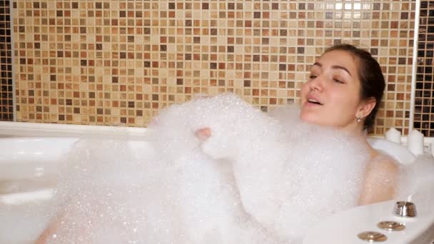 Женщина играет с пеной, когда лежит в ванной — стоковое видео
