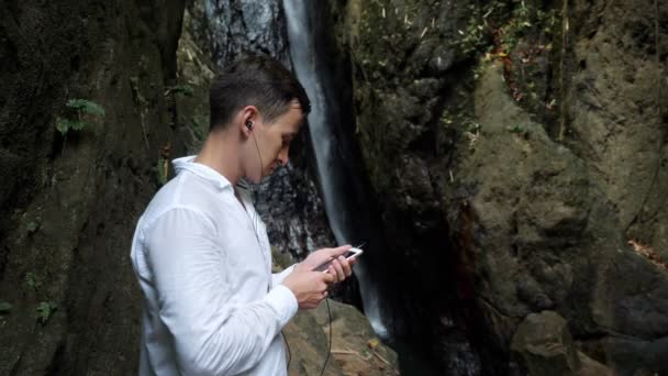 Joven sostiene el teléfono inteligente en la mano y escucha música — Vídeos de Stock