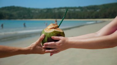 Erkeklerin elleri kumsalda kadınların eline hindistan cevizi uzatır.