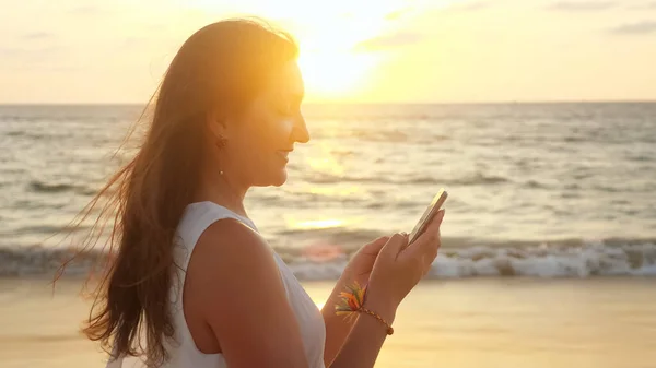 Usmívající se dívka používá smartphone na pláži v tropickém letovisku — Stock fotografie