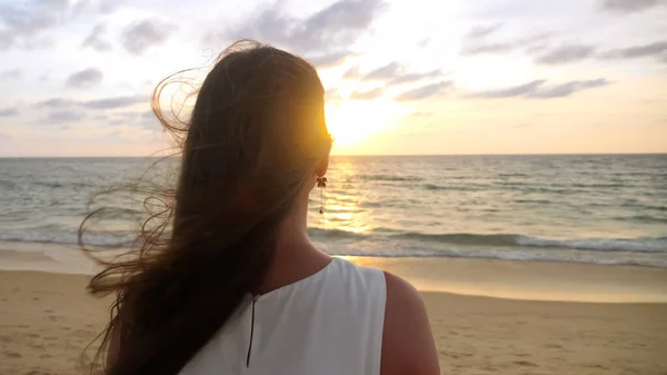 Žena s dlouhými vlasy stojí na pláži oceánu ve větrném večeru — Stock fotografie