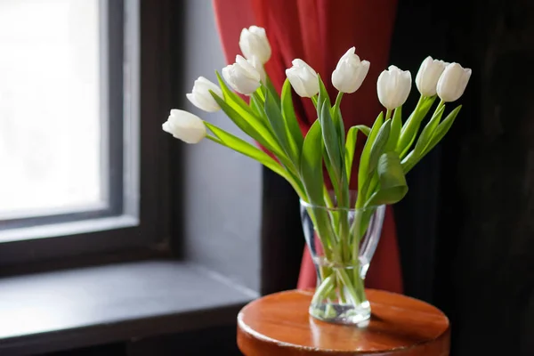 Witte tulpen in een glasvaas op een zwarte en rode achtergrond — Stockfoto