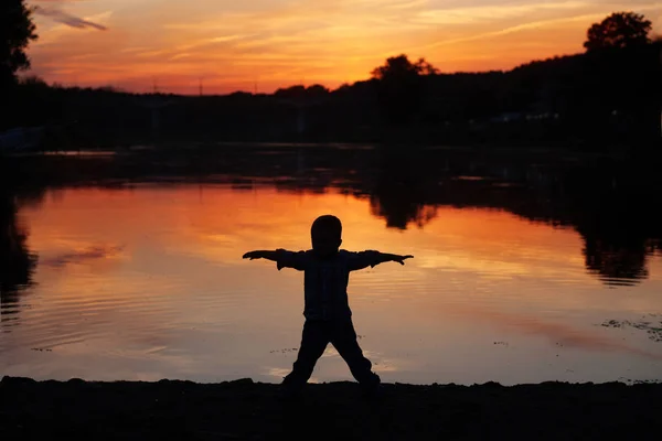 Šťastné dítě siluety stojící na pláži při západu slunce. — Stock fotografie