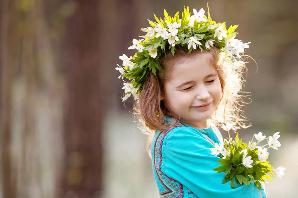 春の木の中を歩く青いドレスを着た美しい少女 頭の上に花からの花輪を持つかわいい女の子の肖像画 夏に屋外で遊んでいる子供 イースターの時間だ スペースのコピー — ストック写真
