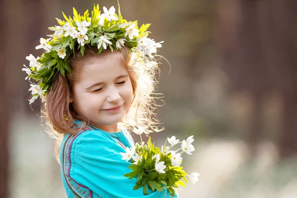 春の木の中を歩く青いドレスを着た美しい少女 頭の上に花からの花輪を持つかわいい女の子の肖像画 夏に屋外で遊んでいる子供 イースターの時間だ スペースのコピー — ストック写真