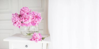 Cam vazoda pembe şakayıklar. Pencerenin yanındaki beyaz bir masada çiçekler. Sabah ışığı odada. Katalog ya da internet mağazası için güzel şakayık çiçekleri. Çiçek dükkanı ve teslimat konsepti. Pankart. Boşluğu kopyala