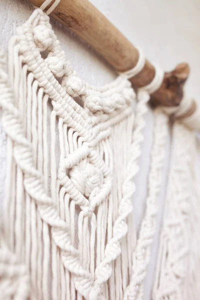 El yapımı makrome% 100 pamuk duvar süslemesi ve beyaz bir duvara asılı tahta sopa. Makrame örgü ve pamuk iplikleri. Ayrıntılar yakın. Kadın hobisi.  