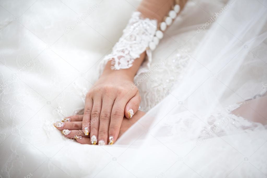 Tender beautiful bride's hands on elegant white wedding dress closeup.