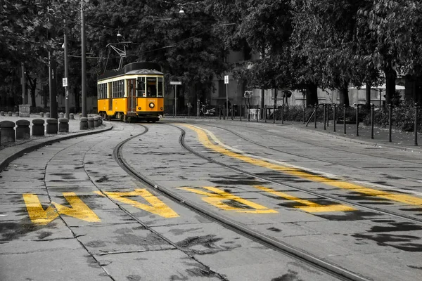 A picture of the typical yellow tram in Milan, Italy, passing throught the city center. The tram is isolated in the black and white background.