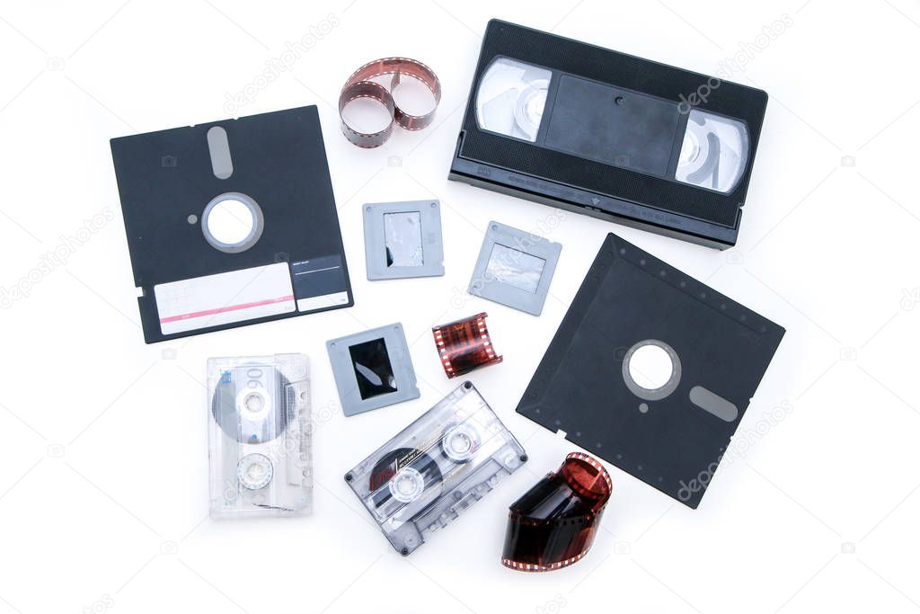 A group of old retro audio visual equipment used to capture or record  pictures, video, audio or data. The floppy disc, audio and video cassettes