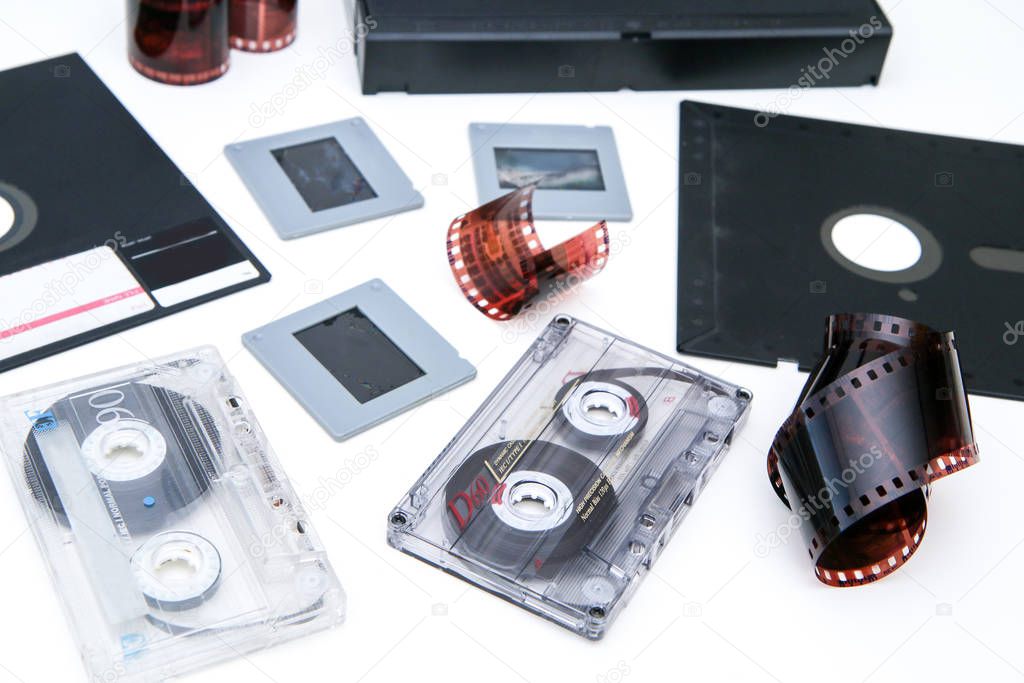 A group of old retro audio visual equipment used to capture or record  pictures, video, audio or data. The floppy disc, audio and video cassettes