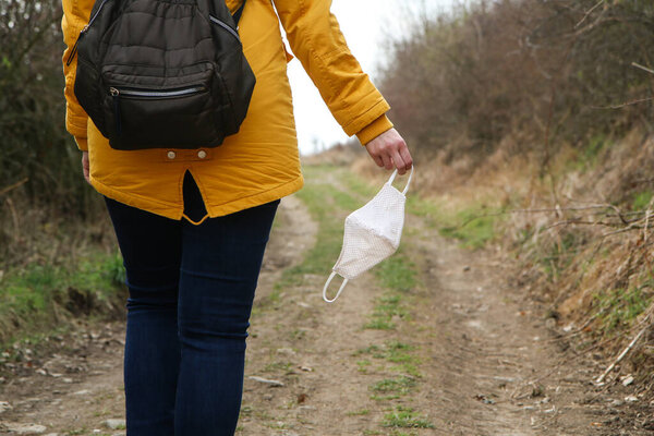 Woman is holding the textile home made face mask used for protection against viruses while walking in the nature. Symbol for protest against regulations or freedom after end of pandemic. 