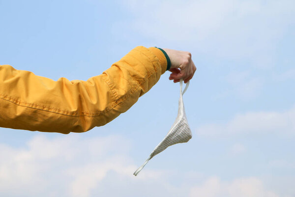Woman is holding the textile home made face mask used for protection against viruses while walking in the nature. Symbol for protest against regulations or freedom after end of pandemic. 