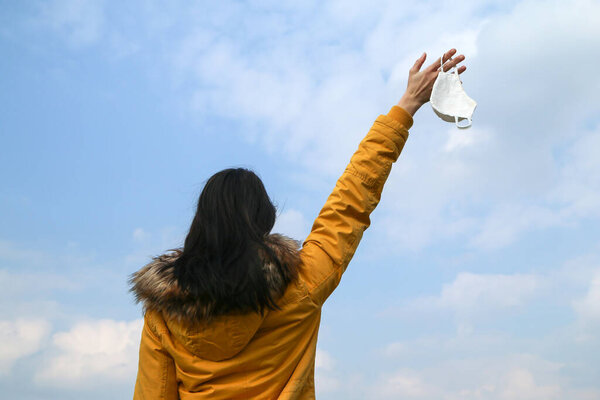 Woman is holding the textile home made face mask used for protection against viruses while walking in the nature. Symbol for protest against regulations or freedom after end of pandemic. 