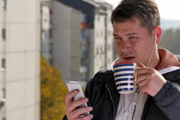 Uomo che utilizza smartphone sul balcone durante la giornata di sole Immagine Stock