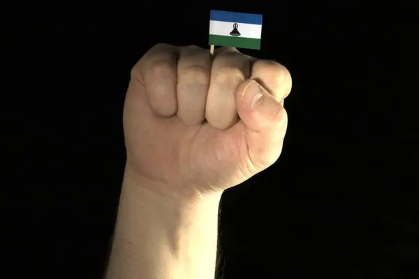 Ο άνθρωπος χέρι γροθιά με σημαία του Λεσότο απομονώνονται σε μαύρο φόντο — Φωτογραφία Αρχείου