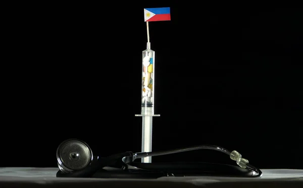 Stetoskop dan jarum suntik diisi dengan obat-obatan yang menyuntikkan bendera Filipina pada latar belakang hitam — Stok Foto