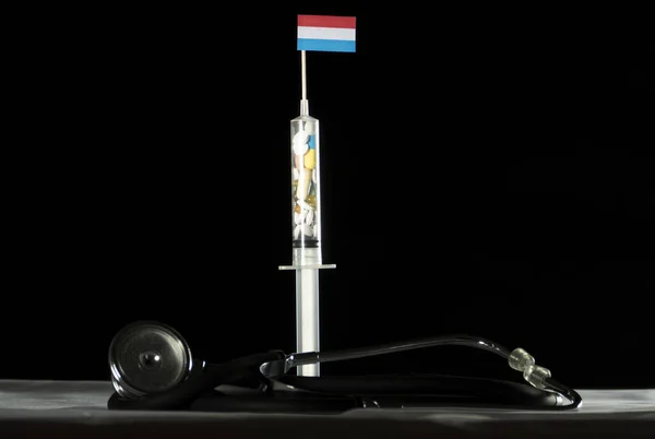 Estetoscópio e seringa cheios de drogas injetando a bandeira do Luxemburgo em um fundo preto — Fotografia de Stock
