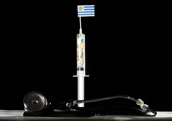 Estetoscopio y jeringa llenos de drogas inyectando la bandera uruguaya sobre fondo negro —  Fotos de Stock