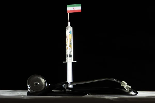 Стетоскоп и шприц, наполненные наркотиками, вводящими иранский флаг на черном фоне — стоковое фото