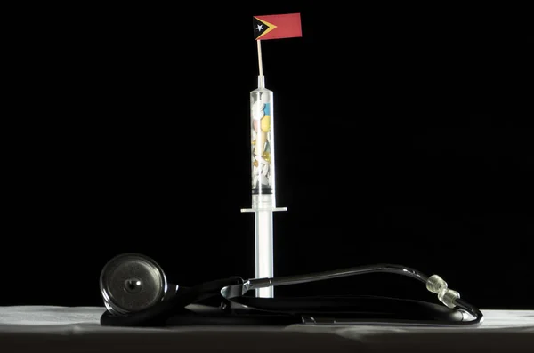 Doğu Timor bayrağı siyah bir arka plan üzerinde enjekte ederek uyuşturucu stetoskop ve şırınga dolu — Stok fotoğraf