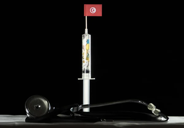 Estetoscópio e seringa cheios de drogas injetando a bandeira tunisiana em um fundo preto — Fotografia de Stock