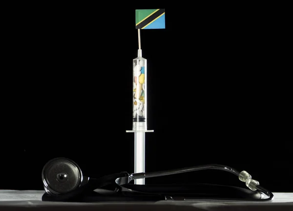 Siyah bir arka plan üzerinde Tanzanya bayrak enjekte ederek uyuşturucu stetoskop ve şırınga dolu — Stok fotoğraf