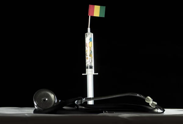Estetoscópio e seringa cheios de drogas injetando a bandeira da Guiné em um fundo preto — Fotografia de Stock