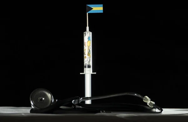 Estetoscópio e seringa cheios de drogas injetando a bandeira das Bahamas em um fundo preto — Fotografia de Stock