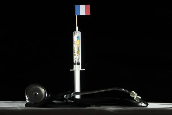 Estetoscópio e seringa cheios de drogas injetando a bandeira francesa em um fundo preto — Fotografia de Stock
