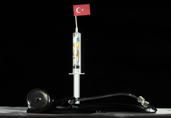 Stethoskop und Spritze gefüllt mit Drogen, die die türkische Flagge auf schwarzem Hintergrund injizieren — Stockfoto