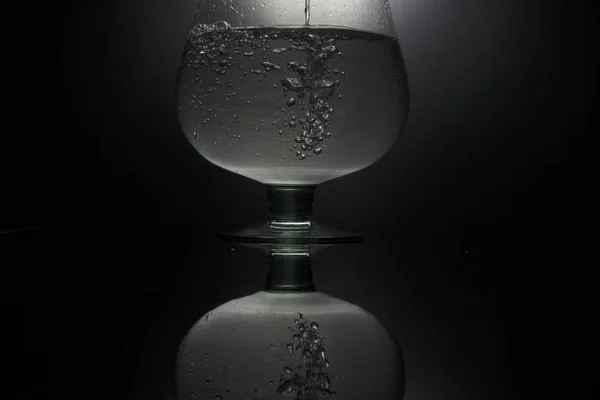 Gieten van water in het glas op zwarte achtergrond — Stockfoto
