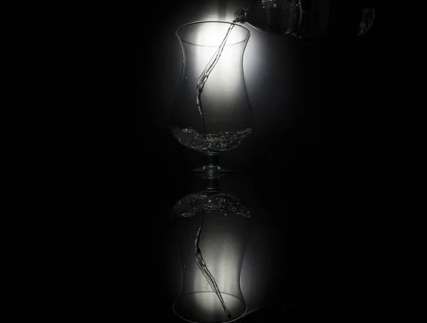 Despejar água em vidro sobre fundo preto — Fotografia de Stock
