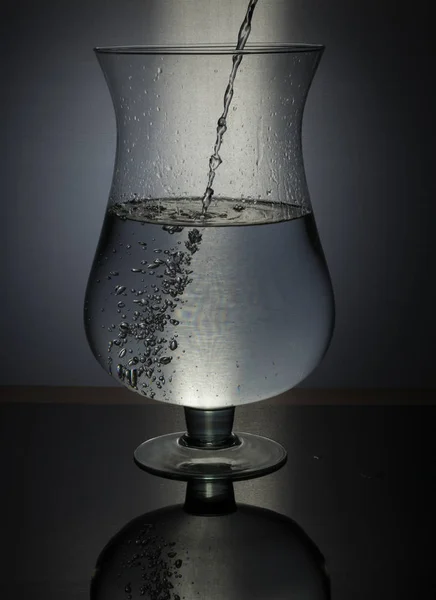 Vylévání vody ve skle na černém pozadí — Stock fotografie