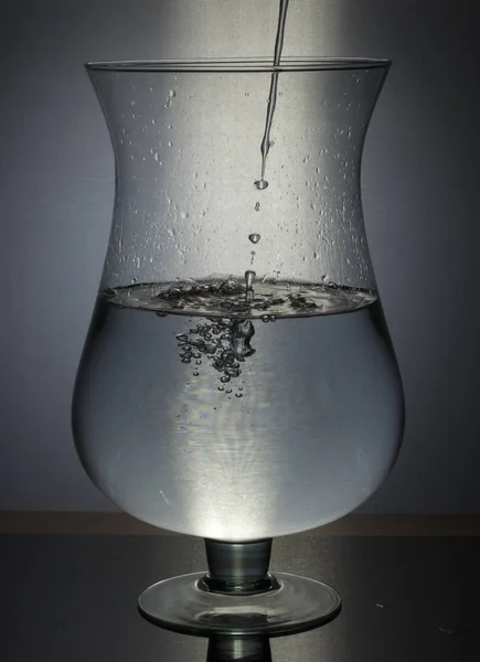 Menuang air dalam kaca pada latar belakang hitam — Stok Foto
