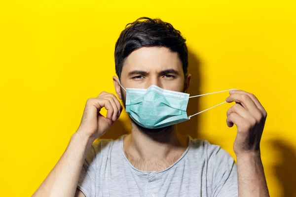 Portrait of young man, takes off the medical flu mask, on background of yellow color.