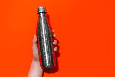 Yeniden kullanılabilir çelik termo şişe. Arkaplanda erkek eli su püskürtülmüş. Lif rengi.