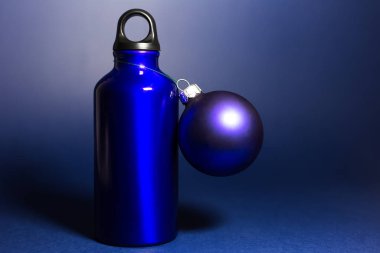 Yeniden kullanılabilir mavi renk, alüminyum termo su şişesi ve koyu arkaplanda bir Noel topu..