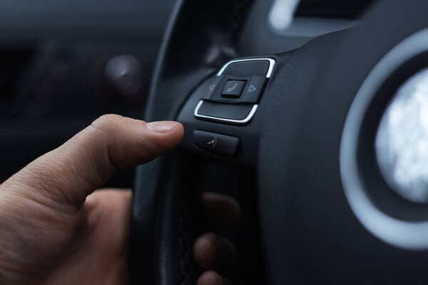 Close-up of male hand presses button of phone on steering wheel of car.
