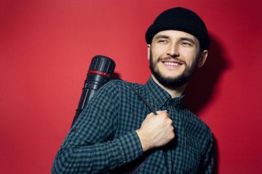 Genç modern mimarın portresi, kırmızı arka planda izole edilmiş çizim tüpü taşıyan gülümseyen adam..