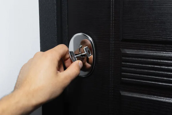 Close-up of male hand unlocking or locking lock of modern house door with key.