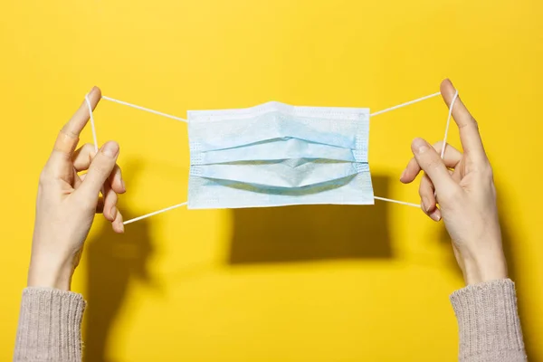 Close Mãos Femininas Segurando Máscara Médica Isolado Fundo Amarelo — Fotografia de Stock