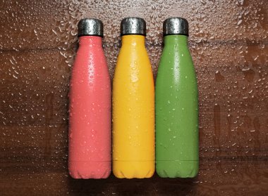 Mercan pembesi, yeşil soğan, sarı güneş ışığı veya çeliğin safran rengi termo eko şişe ahşap masa üzerine su püskürtülmüş..