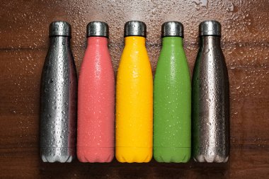 Mercan pembesi, yeşil soğan, sarı güneş ışığı ya da safran rengi ve ahşap masa üzerindeki sıvı için gri termo eko şişe..