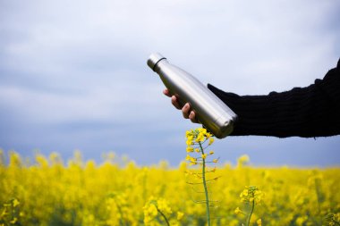 Elde paslanmaz termos şişesi, kolza tohumu tarlasında.