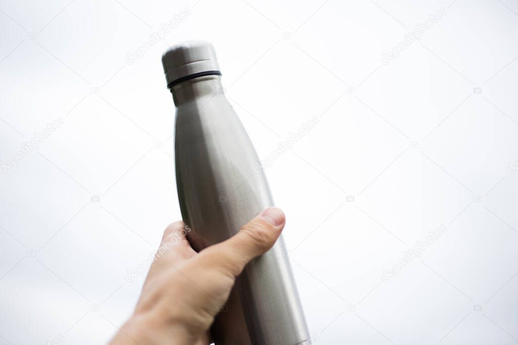 Stainless thermos bottle in man hand isolated on white background